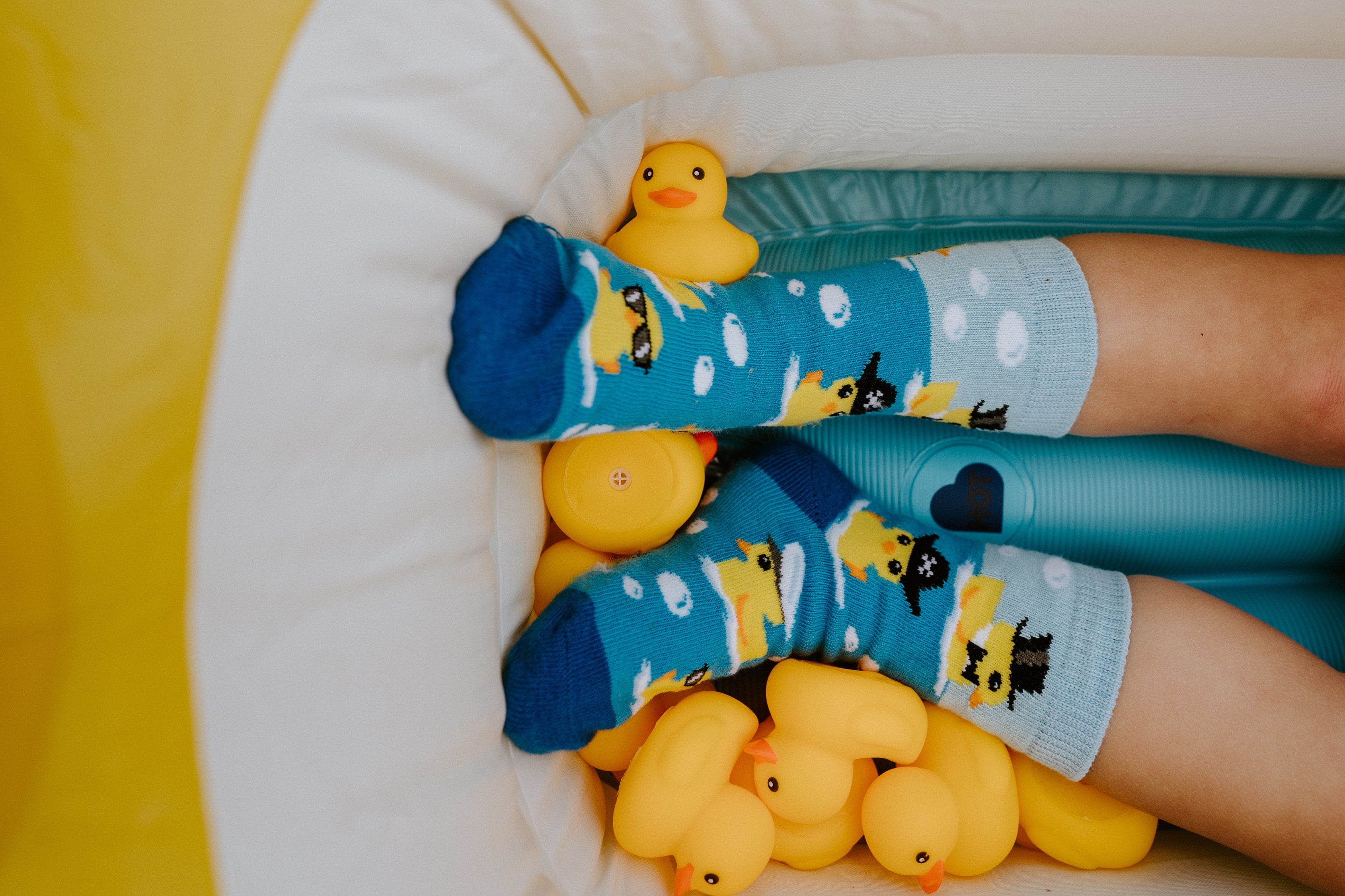 "child model wearing ahoy rubber ducky kids socks, sitting in floaty with rubber duck toys"