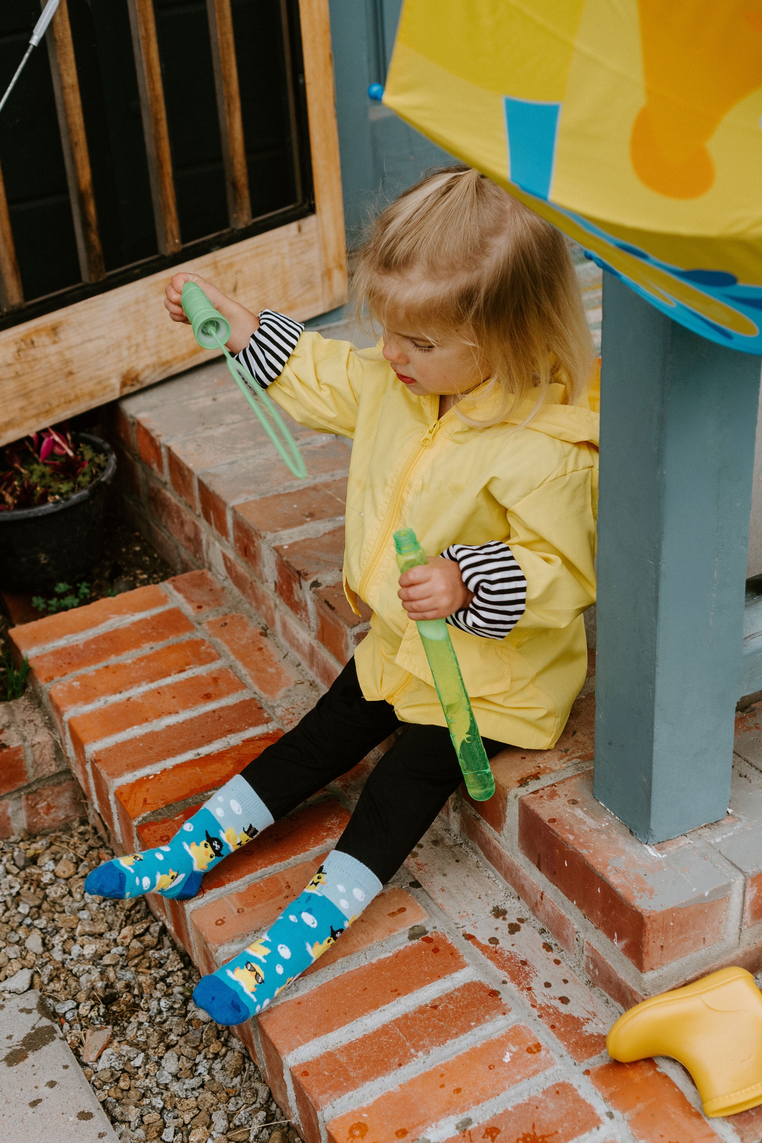 "child sitting on brick steps playing with bubbles wearing ahoy rubber ducky kid's socks"