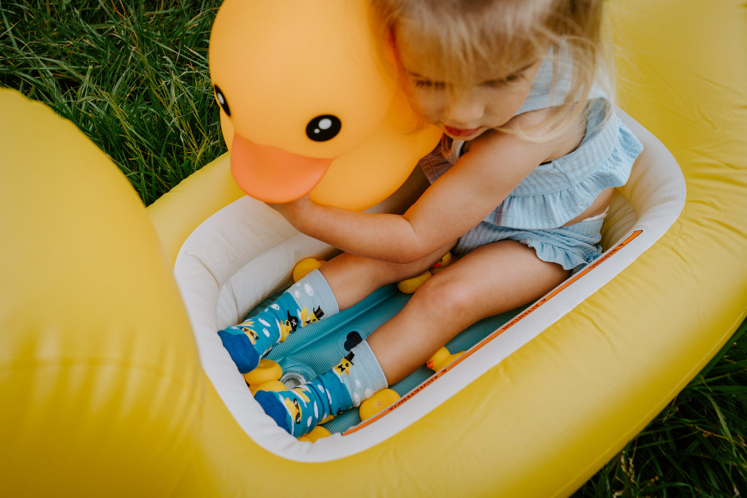 Child playing with a yellow inflatable duck toy on grass and wearing cute rubber ducky socks