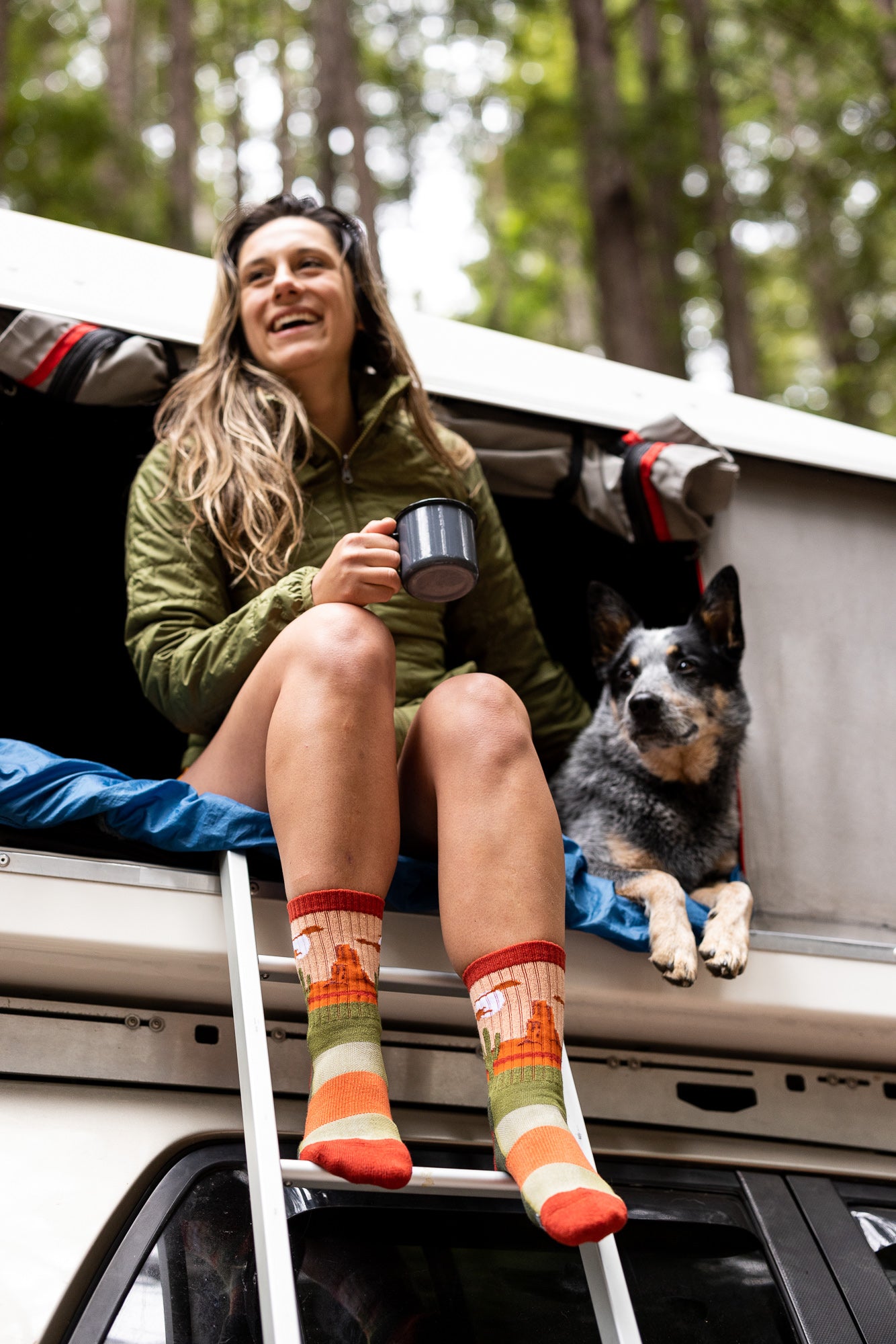 "woman sitting next to pet dog in camper shell wearing compass desert plains socks"