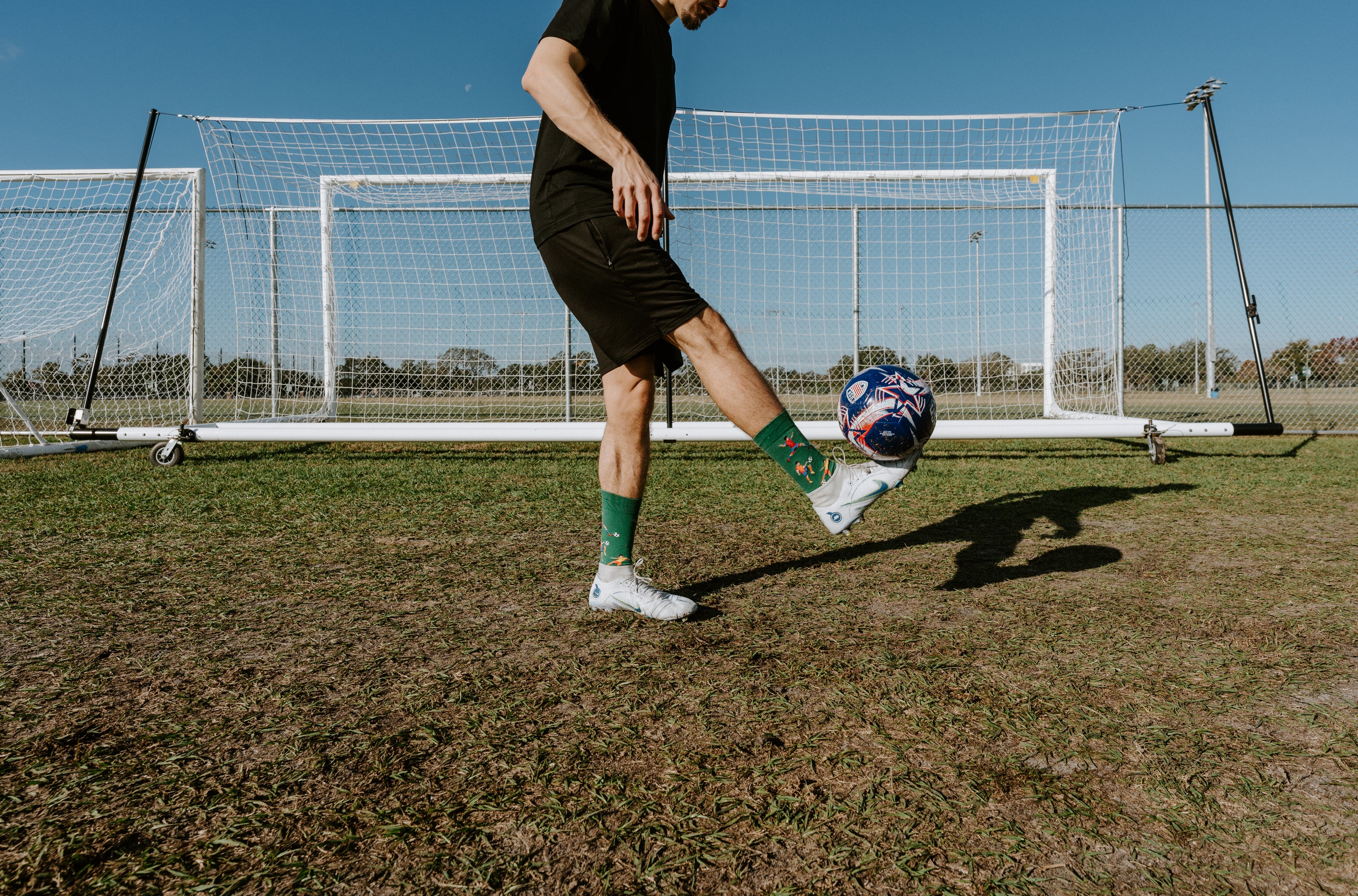 A man juggles a soccer ball while wearing Kicking It socks