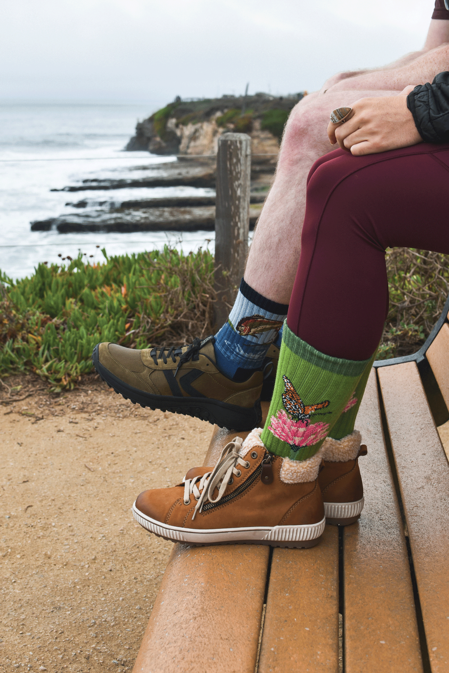 A close-up lifestyle shot of two people, one wearing fish-themed Merino wool socks and the other wearing Merino wool socks with a butterfly and flower on.