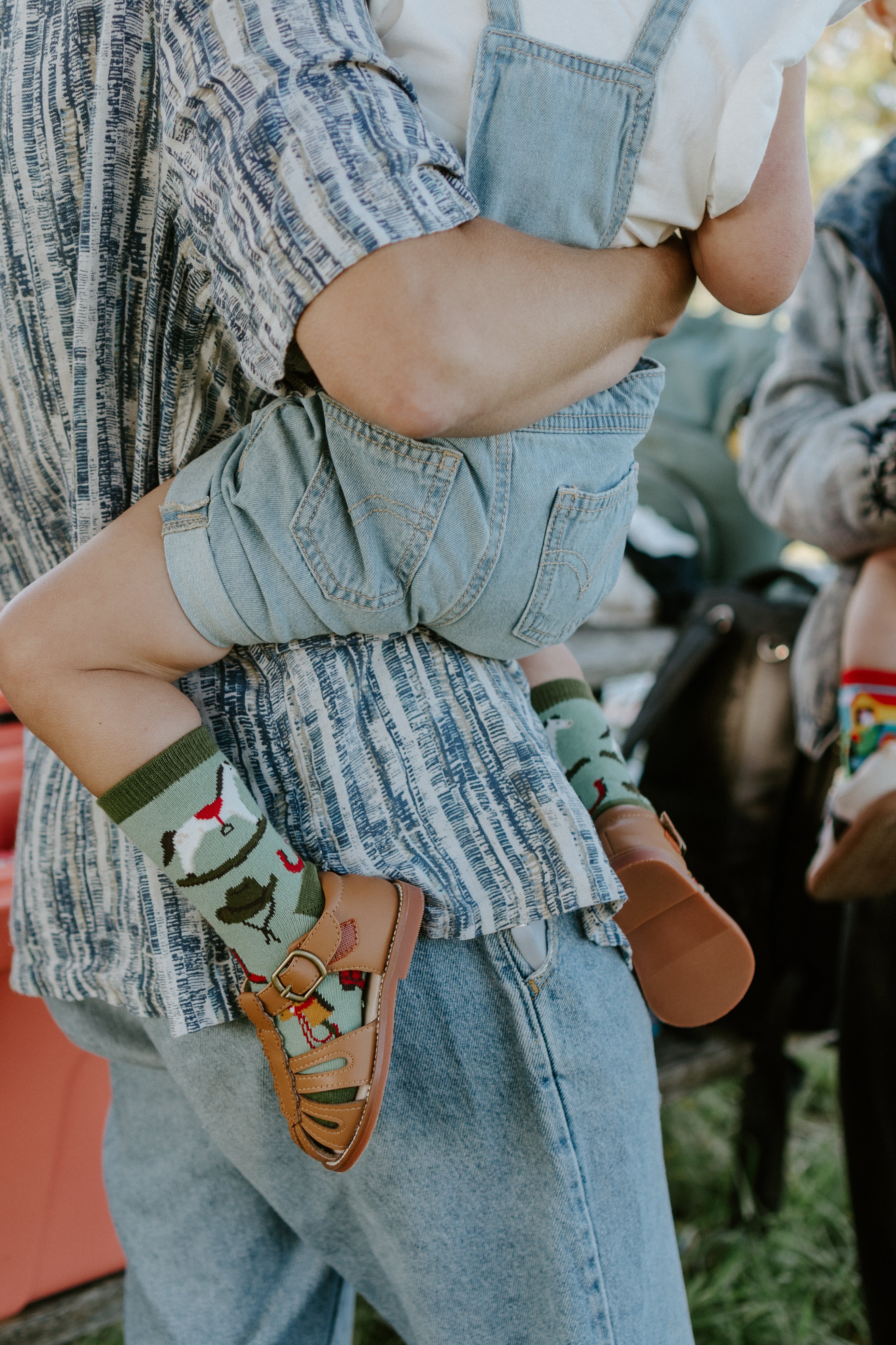 "child being held by adult, child wearing pony up kids socks"