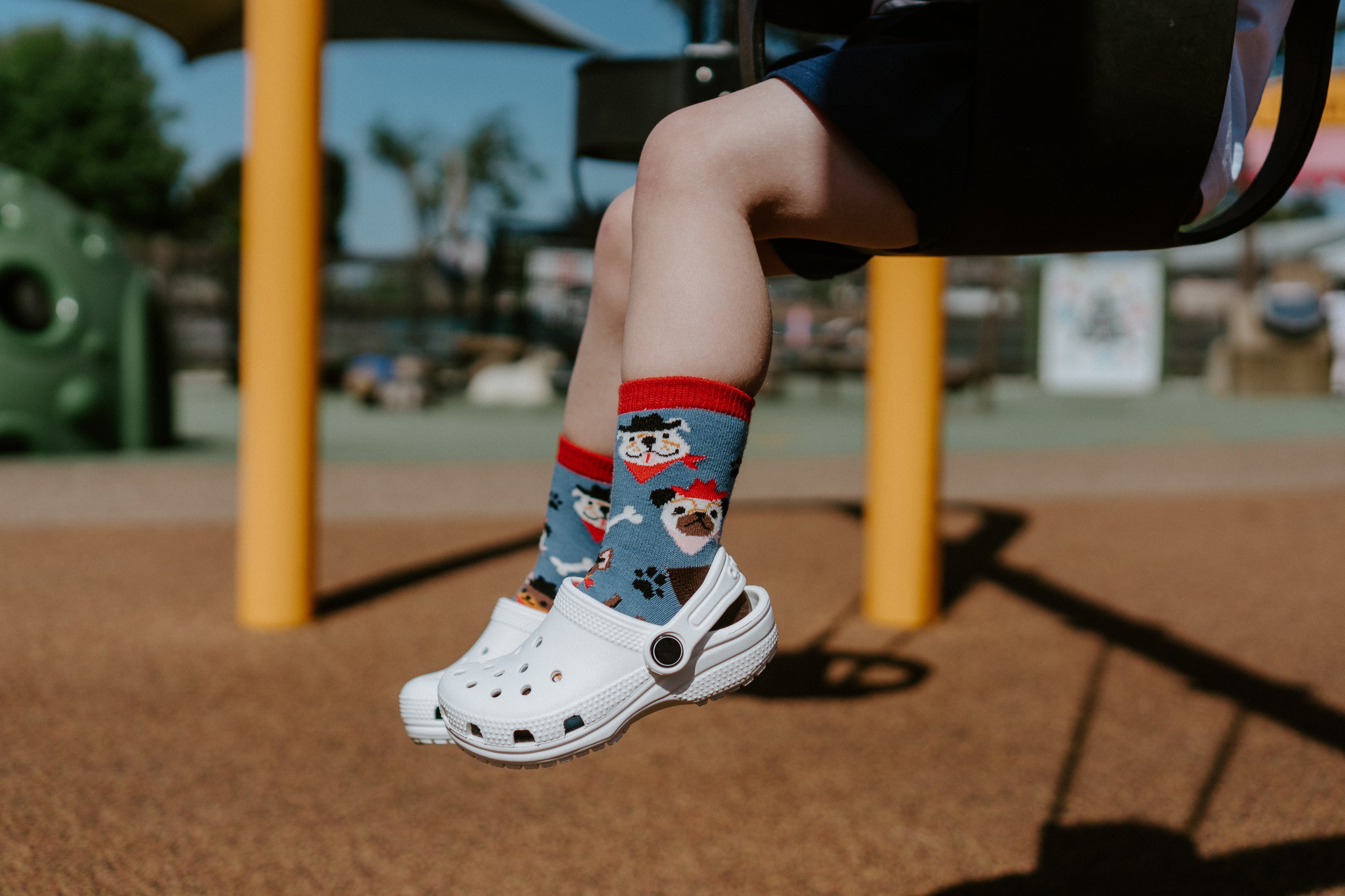 "child model in playground swing wearing saddle up pups kids socks"