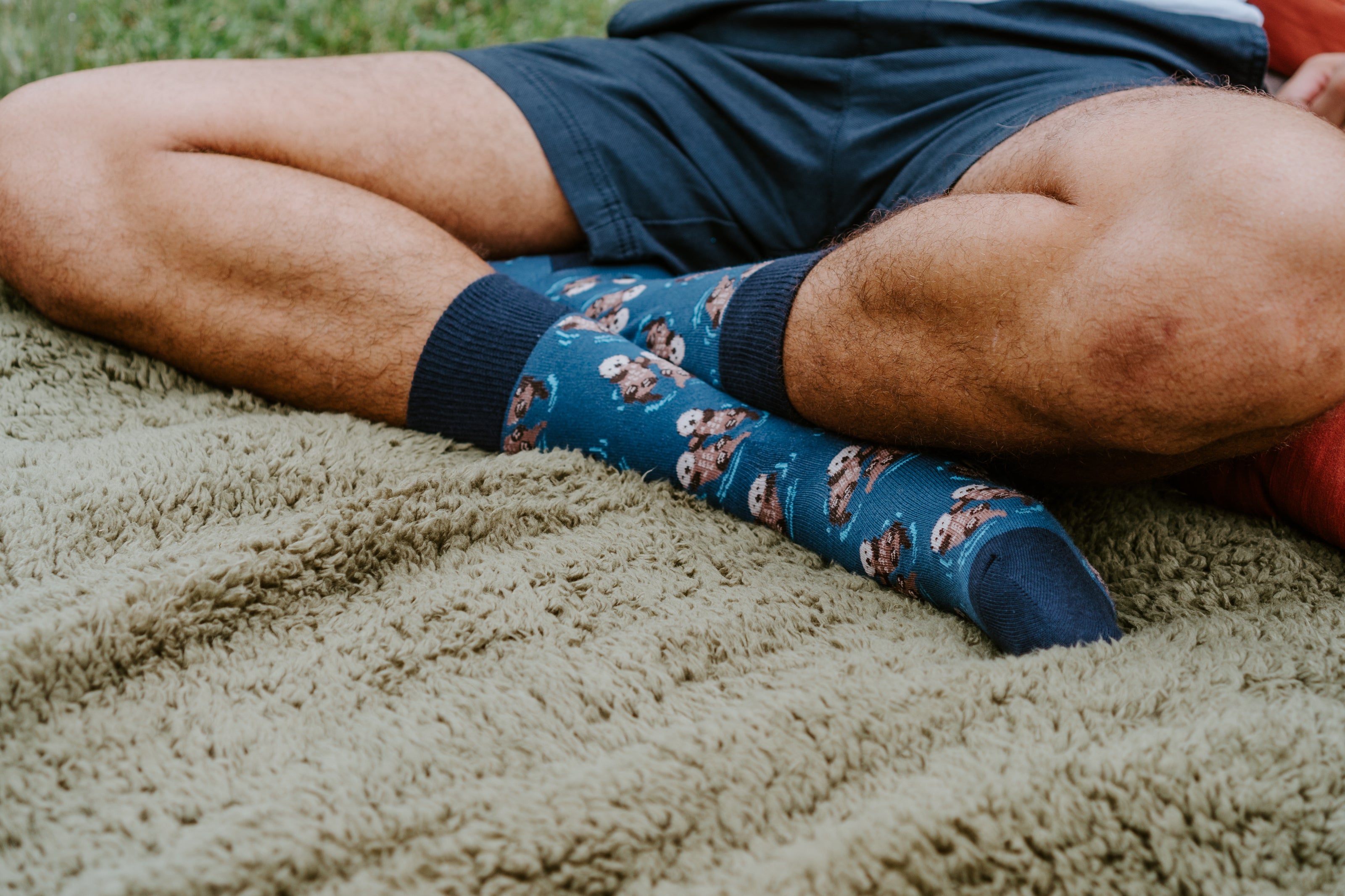 Close-up of person wearing Significant Otter socks sitting on fluffy blanket