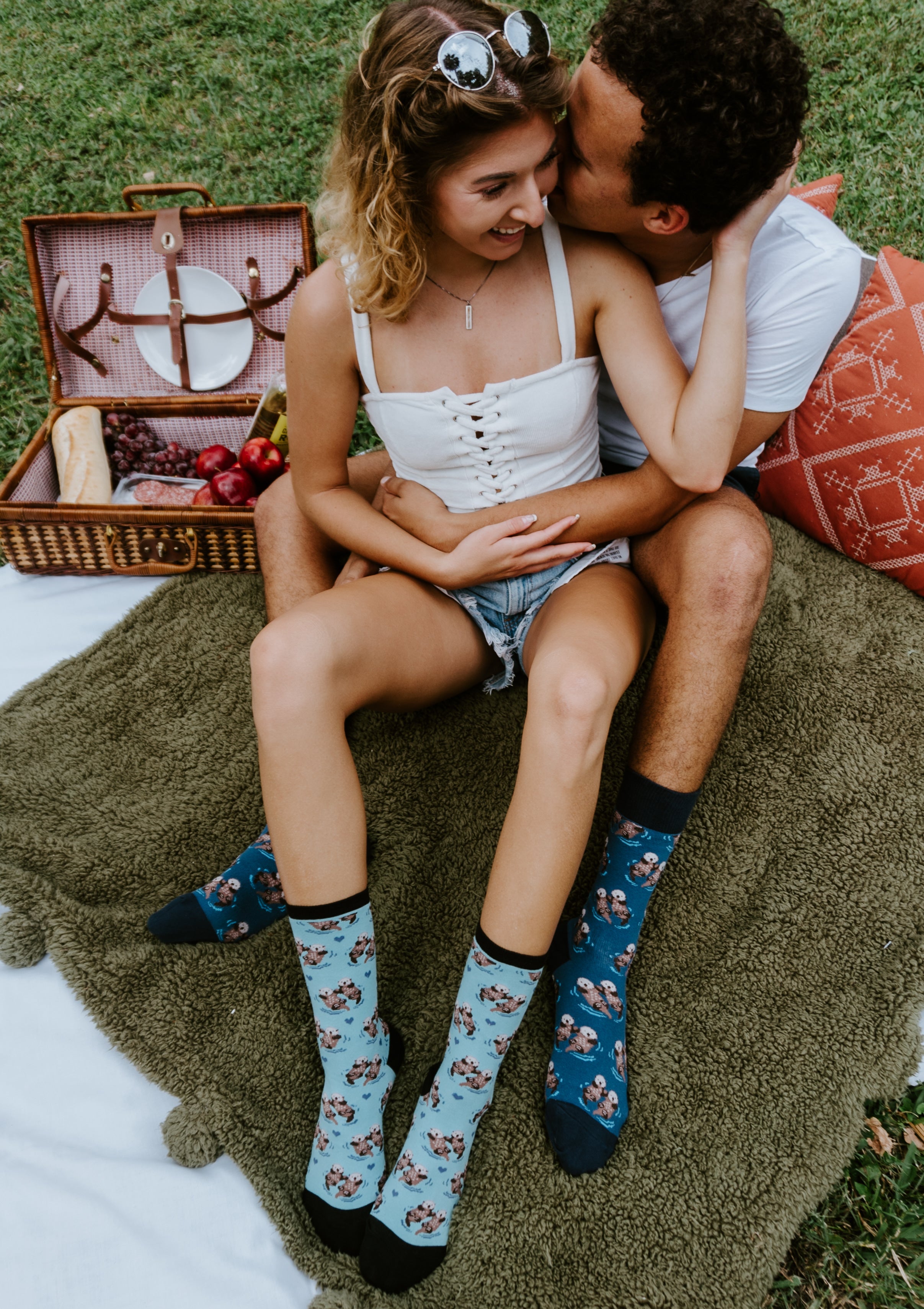Couple sitting on a blanket outdoors with picnic basket, holding hands and smiling wearing Significant Otter socks