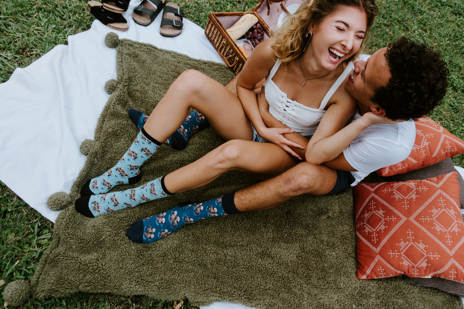 Couple lying on a blanket outdoors, laughing and enjoying each other's company, wearing Significant Otter Socks.