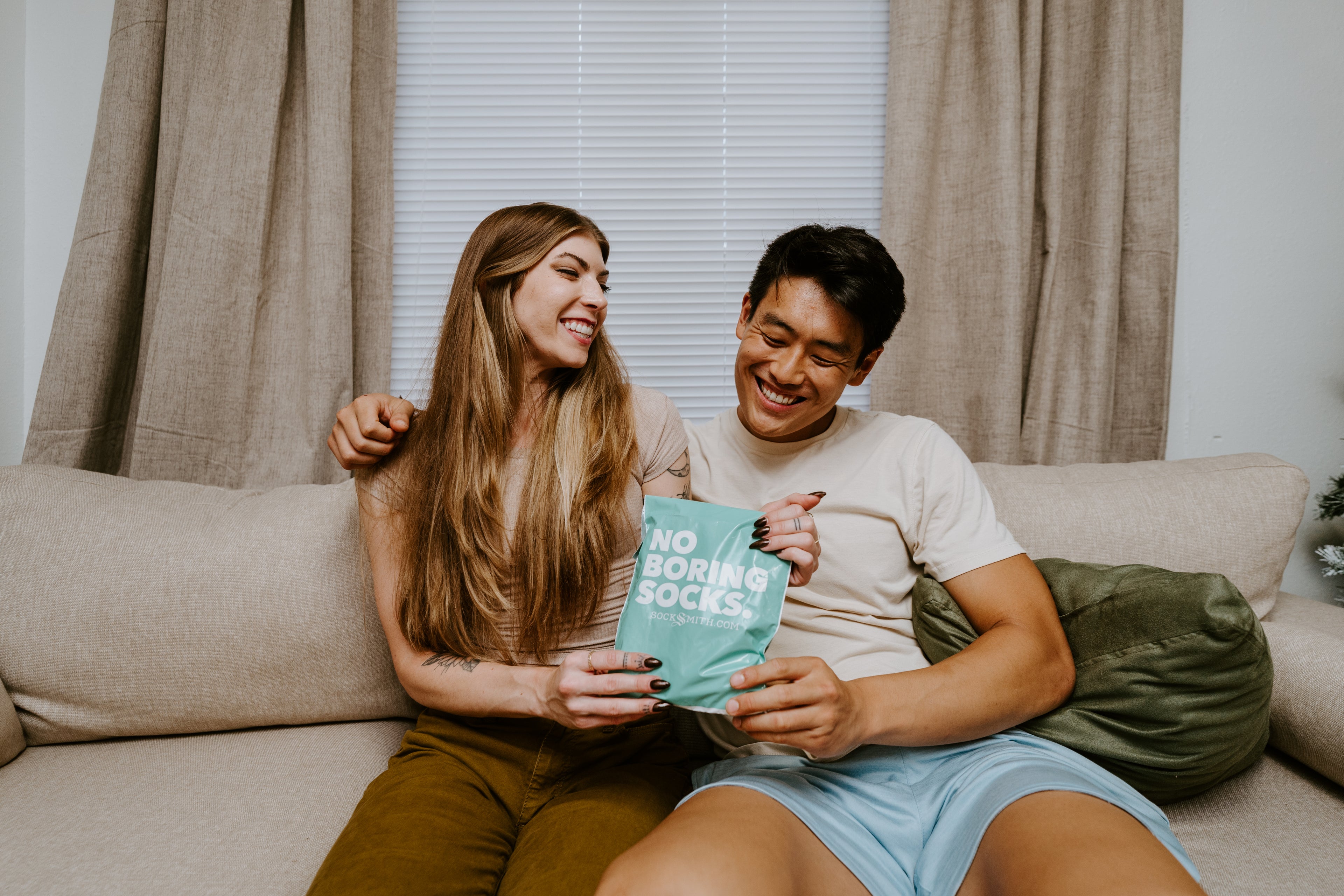 "couple on couch both holding a 'no boring socks' package"