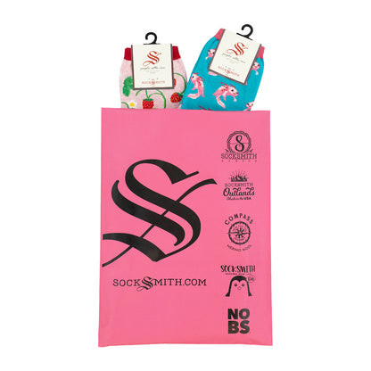 A pink Socksmith gift bag with black printed logos and text, holding two packaged pairs of women's cotton novelty socks.